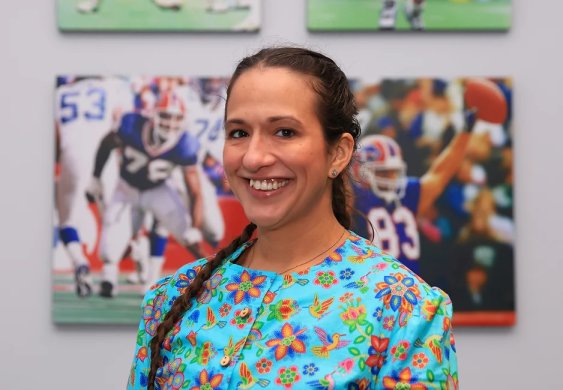 A woman with long braided hair wearing a blue dress smiling