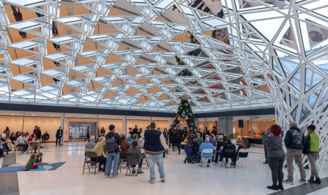 People gathered around a large Christmas tree under a glass mosaic ceiling