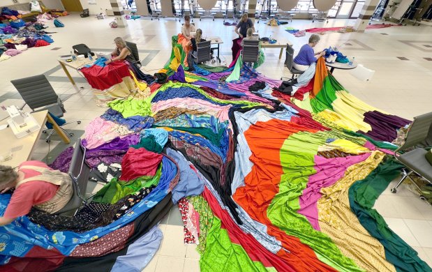 Multiple people at sewing machines sewing one massive swath of vibrant colored fabric