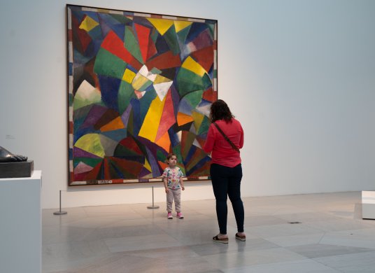 An adult taking a photo of a small child in front of a colorful painting 