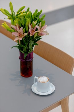 A bouquet of flowers in a vase with a cup of coffee next to it