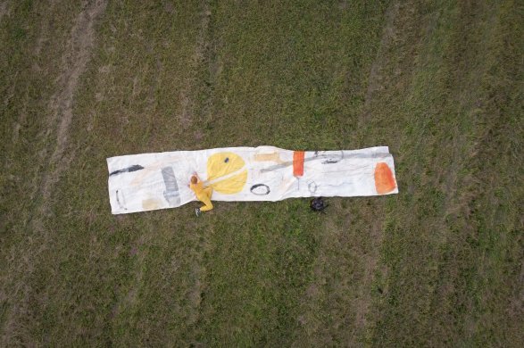 A person painting on a large strip of canvas on a lawn