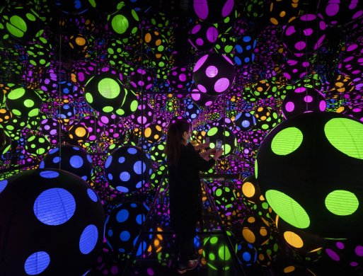 A Mirror Room installation that is dark with various black circles with colorful polka dots on them throughout 