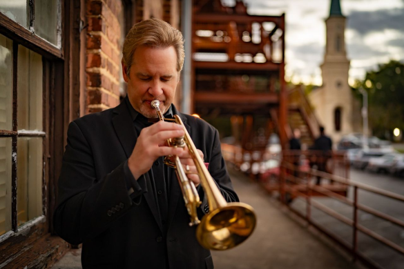A person playing a trumpet with a cityscape in the background