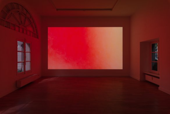 A dark gallery space with a large LED screen lit up in shades of red