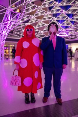 Two people in costume, one with polka dots and the other in a suit with an apple in front of his face