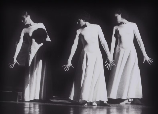 Three women in white dresses dancing with their arms at their sides