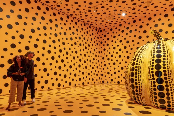 Visitors in an all orange room with black polka dots floor to ceiling with a dotted pumpkin in the center of the space