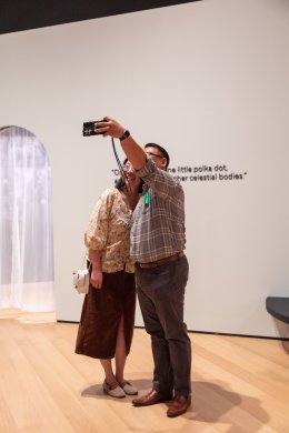 Two people smiling for a selfie on their smartphone in a gallery