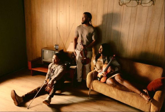 Three people lounging around a couch area with instruments