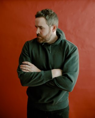 A person looking down in a green hoodie in front of a red background