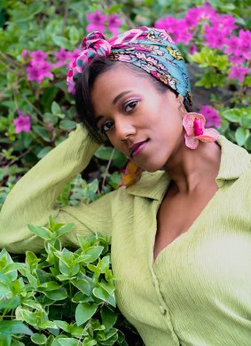 A woman with a floral head wrap in front of vibrant pink flowers