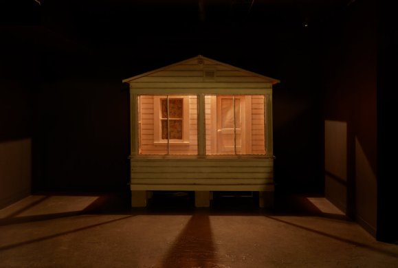 A cabin installation in a dark room with light seeping through the windows