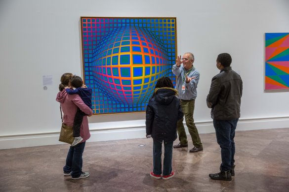 Two families on a tour in front of Victor Vasarely's Vega-nor, a colorful op art painting