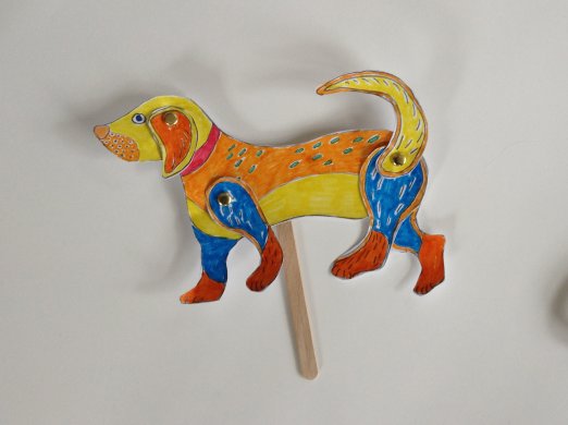 A colorful paper dog puppet on a popsicle stick
