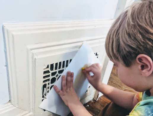 A boy holding a paper over a heating vent and rubbing a crayon on it