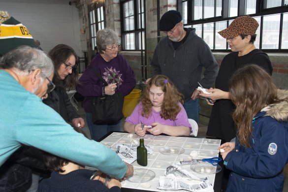 Kids and adults molding white clay into seashell shapes around a square white table
