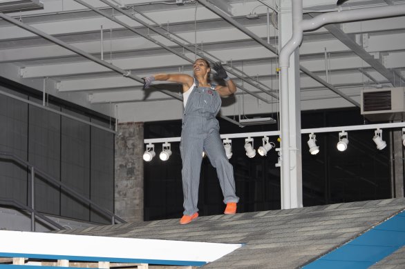 A woman in overalls dancing on a rooftop