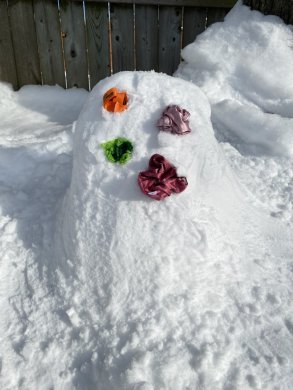 A mound of snow with balls or orange, green, lavender, and magenta fabric stuck in the side like polka dots