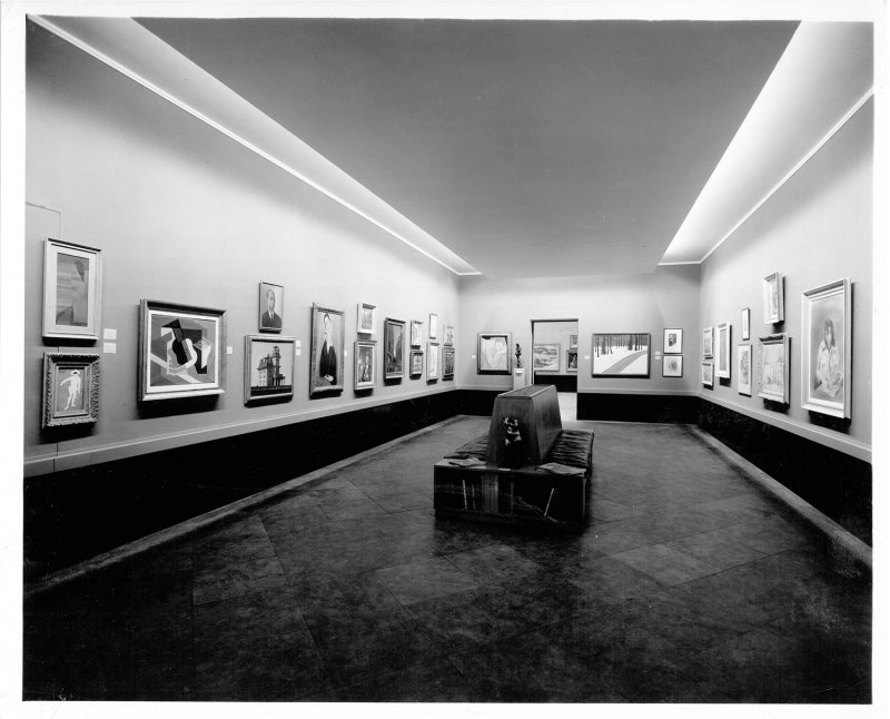 A black and white photograph of a gallery with paintings hanging on the walls