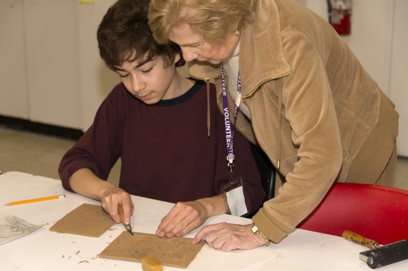 An older woman helping a young boy with an artmaking project in the classroom