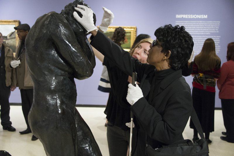 A tour guide and visitor touching a sculpture with white gloves on