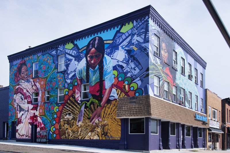 A large mural spanning two exterior walls of a building featuring three Latinx women