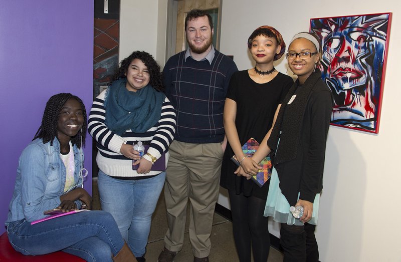 Five teens, one sitting and four standing, in front of an artwork