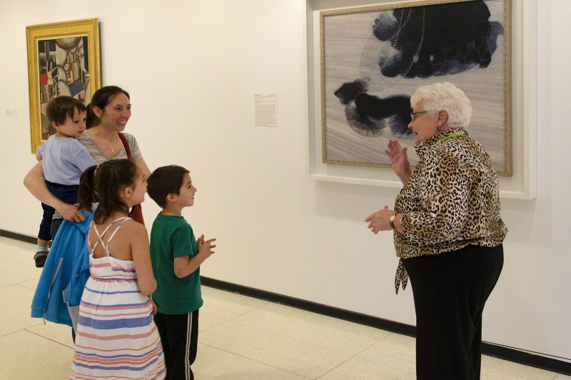 A family on a tour in front of a painting of a woman walking a dog