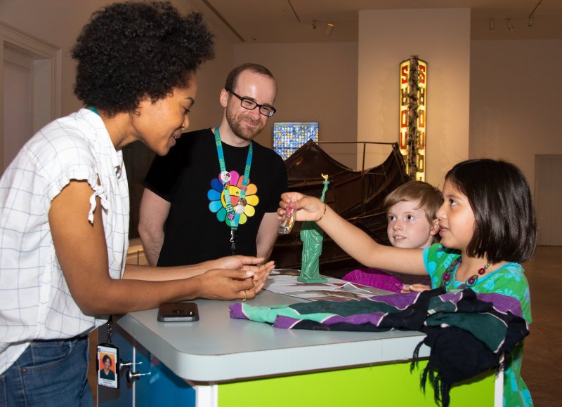 An African American woman and a white man help kids with materials on the ArtCart