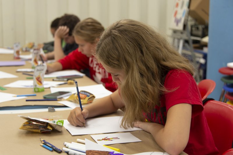 Four young teens making comic book drawings at a long table