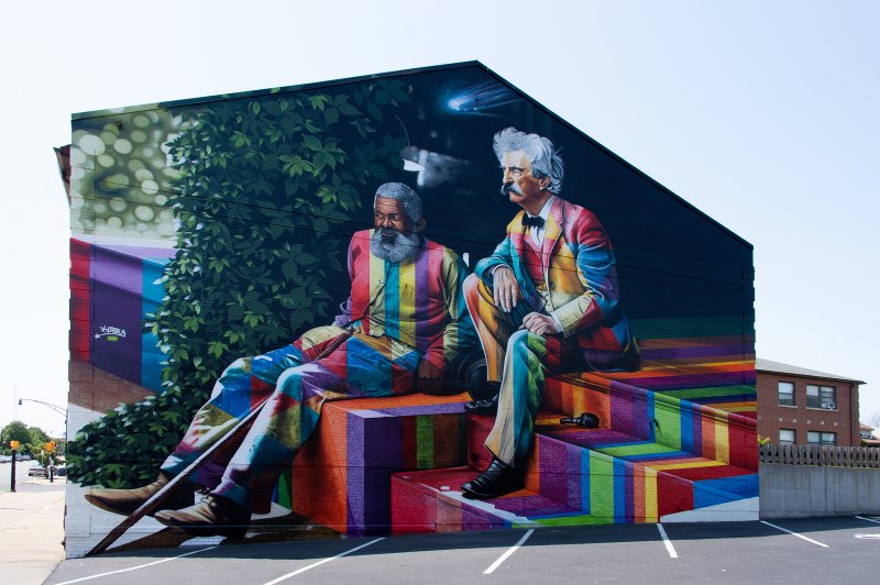 A large colorful mural of an African American man and a white man sitting next to each other on steps
