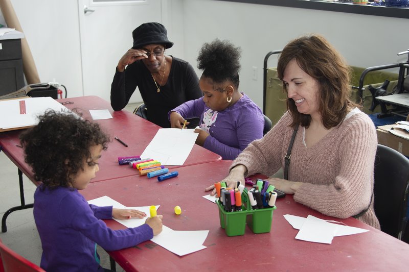Two women and two young girls sitting at a long table making art