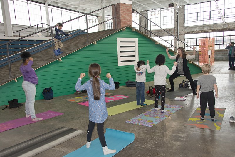 A woman leading a group of kids on yoga mats in a yoga pose