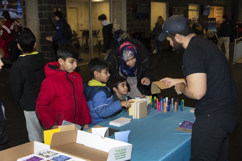 A Latino man handing art supplies to a non-white woman and two kids across a table