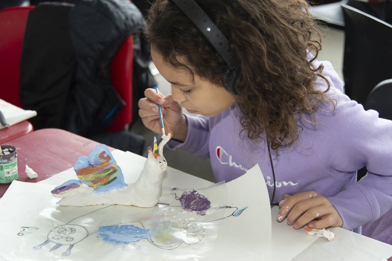 A girl with curly hair painting a sculpture