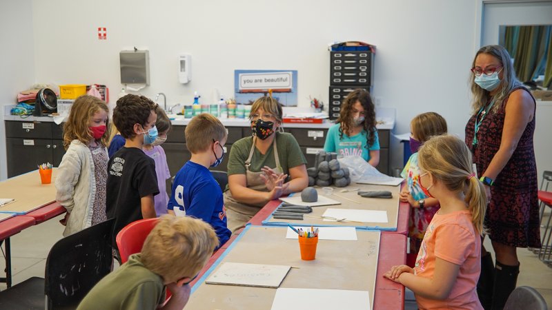 Kids gathered around a teacher showing how to shape clay in her hands