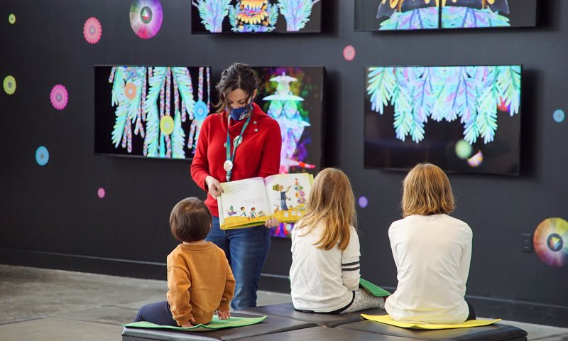 Three kids listening to a woman read a book