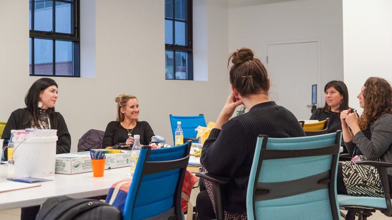 Five women sitting around a table with art supplies on it