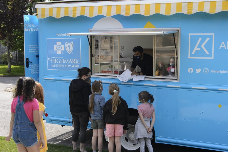 Adults and kids lined up to get art activities from a big blue truck