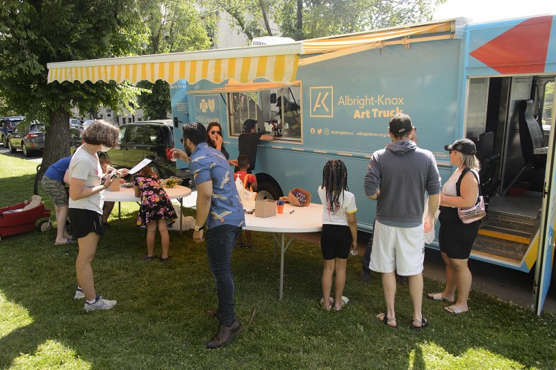 People standing and sitting at tables in front of a big blue truck