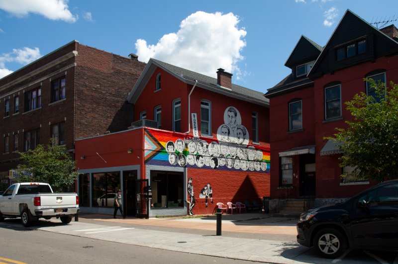 A mural with paintings of different people's faces in black and white with a rainbow background