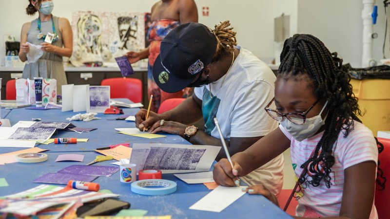 A Black man and woman making art at a long table