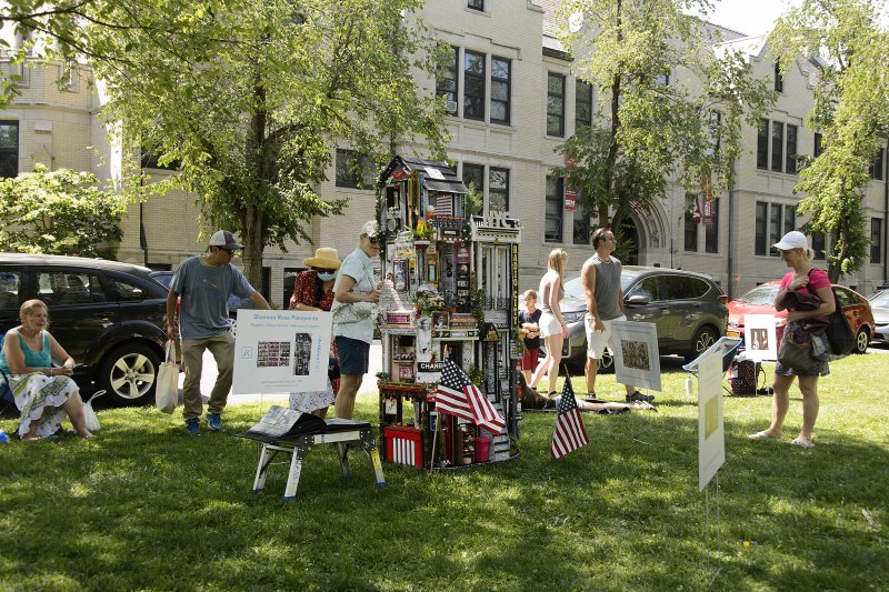 A large re-creation of a New York City townhouse set up on a green grassy area with people around it looking at it