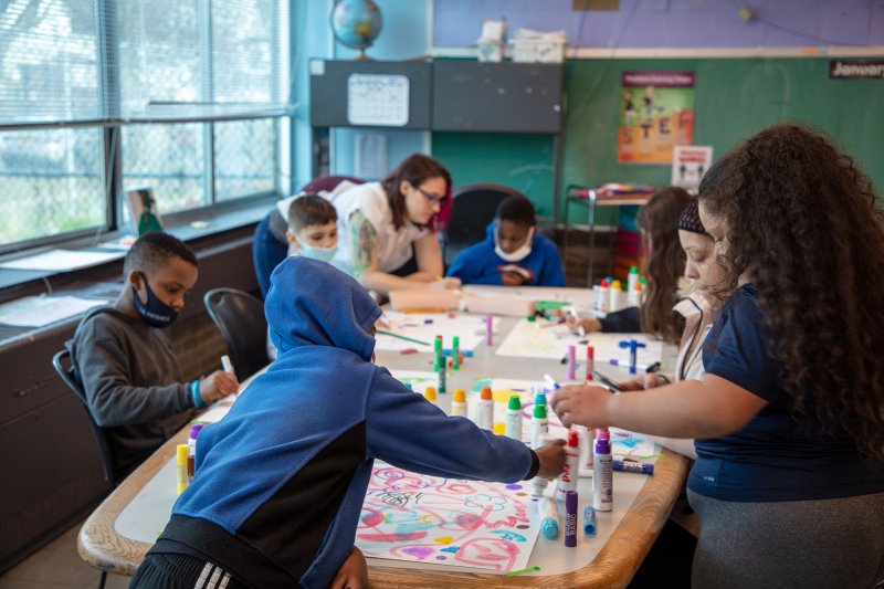 A group of children drawing with markers on large sheets of white paper