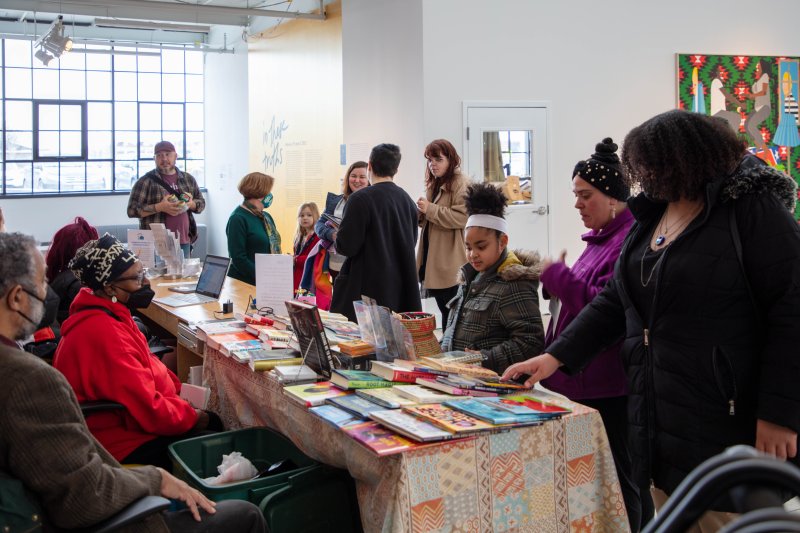 A diverse group of people gather around a table with an array of books on it