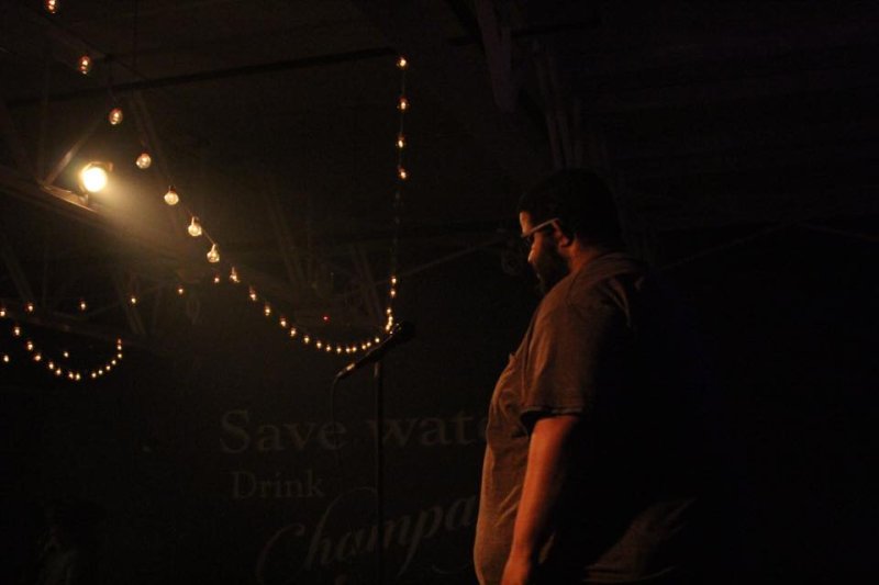 A man of medium dark skin tone stands facing left, a string of lights illuminates him