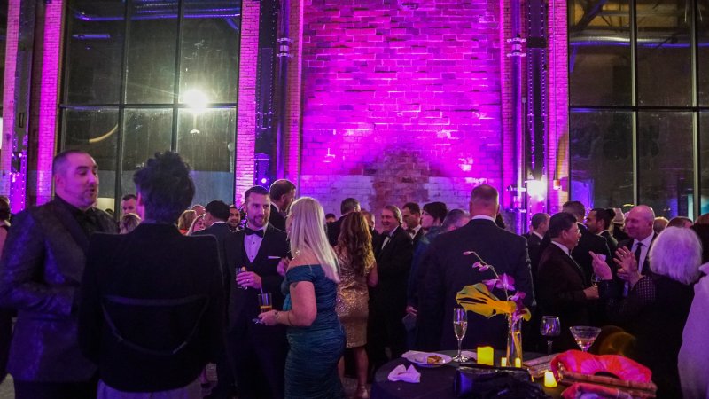 Revelers at a formal cocktail party in a brick industrial space, illuminated in purple light