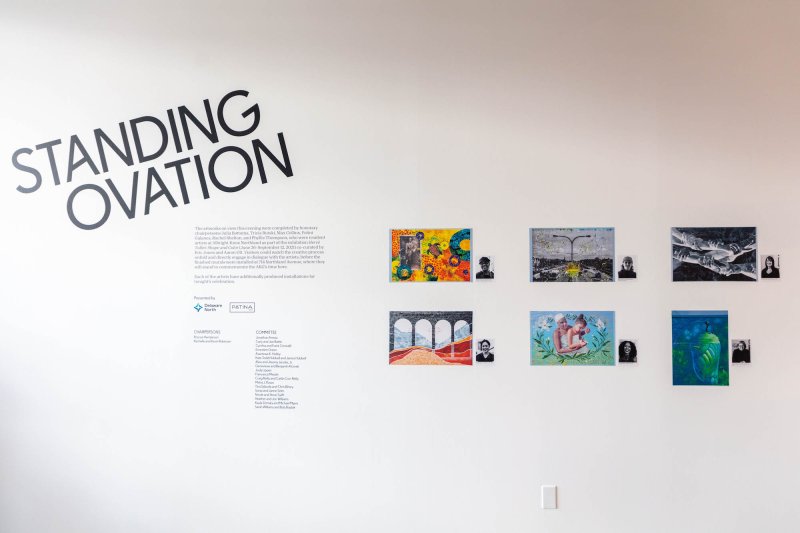 White wall showing Standing Ovation title graphic and photographs of six artist murals