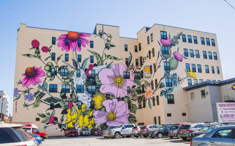 Mural on a large cream colored building of various wildflowers in shades of pink, purple, green and yellow
